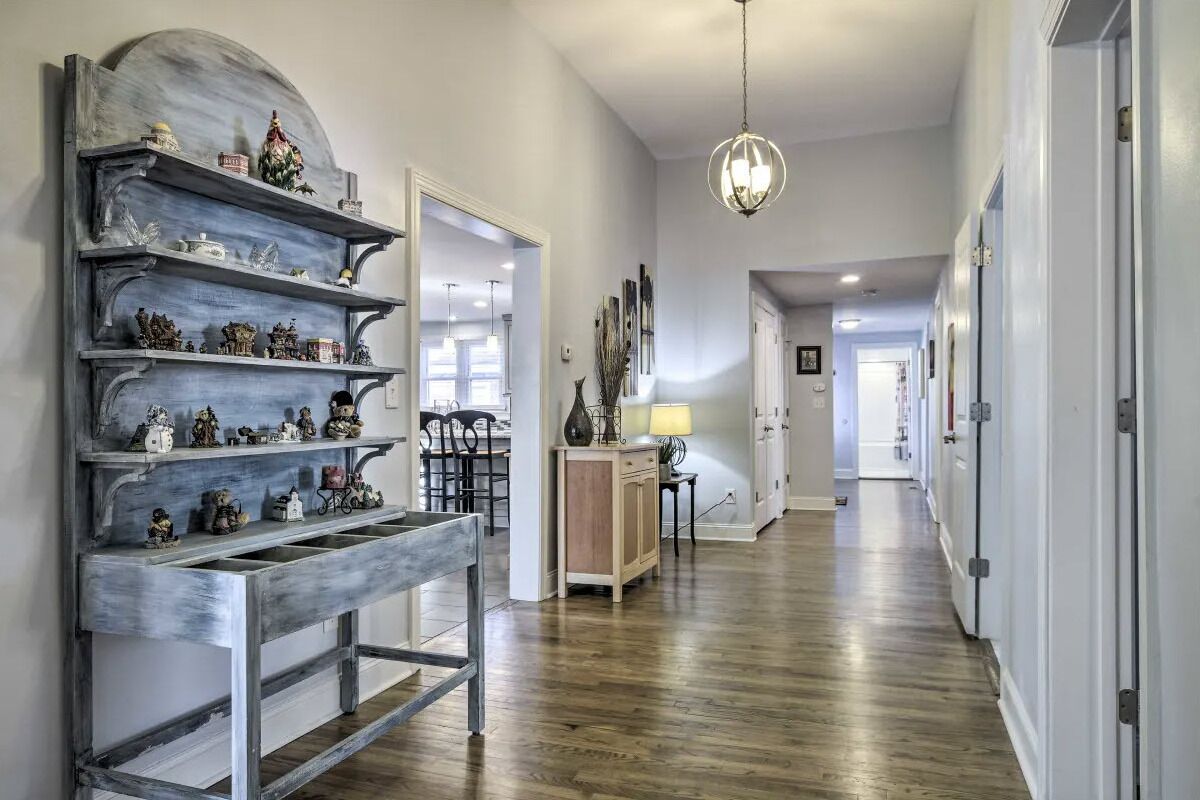 A hallway with wooden flooring, a decorative metal shelf with figurines, a hanging light fixture, and a door leading to another room.