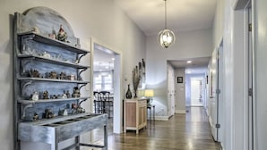 A hallway with wooden flooring, a decorative metal shelf with figurines, a hanging light fixture, and a door leading to another room. - Cottage on the Boulevard - Renovated, Historic Downtown Wendell-3 Beds, 2 Baths (Wendell)