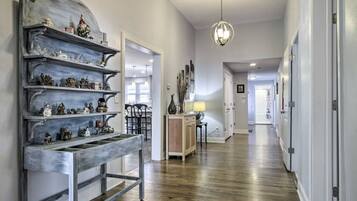 A hallway with wooden flooring, a decorative metal shelf with figurines, a hanging light fixture, and a door leading to another room.