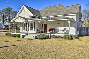 A white two-story house with a covered porch, a red door, and a small outdoor seating area.