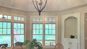 A dining room with a round table, six wooden chairs, a chandelier, and large windows with a view of greenery. - Location!! Pis Nat F., DuPont, Brev. & Ash. 5 bedrooms, 3.5 baths, Sleeps 16! (pisgah forest)