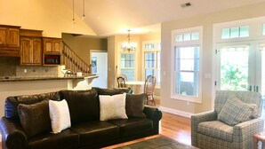 A living room with a black leather sofa, a plaid armchair, and a wooden coffee table. A kitchen with wooden cabinets and a microwave is visible in the background. - Location!! Pis Nat F., DuPont, Brev. & Ash. 5 bedrooms, 3.5 baths, Sleeps 16! (pisgah forest)