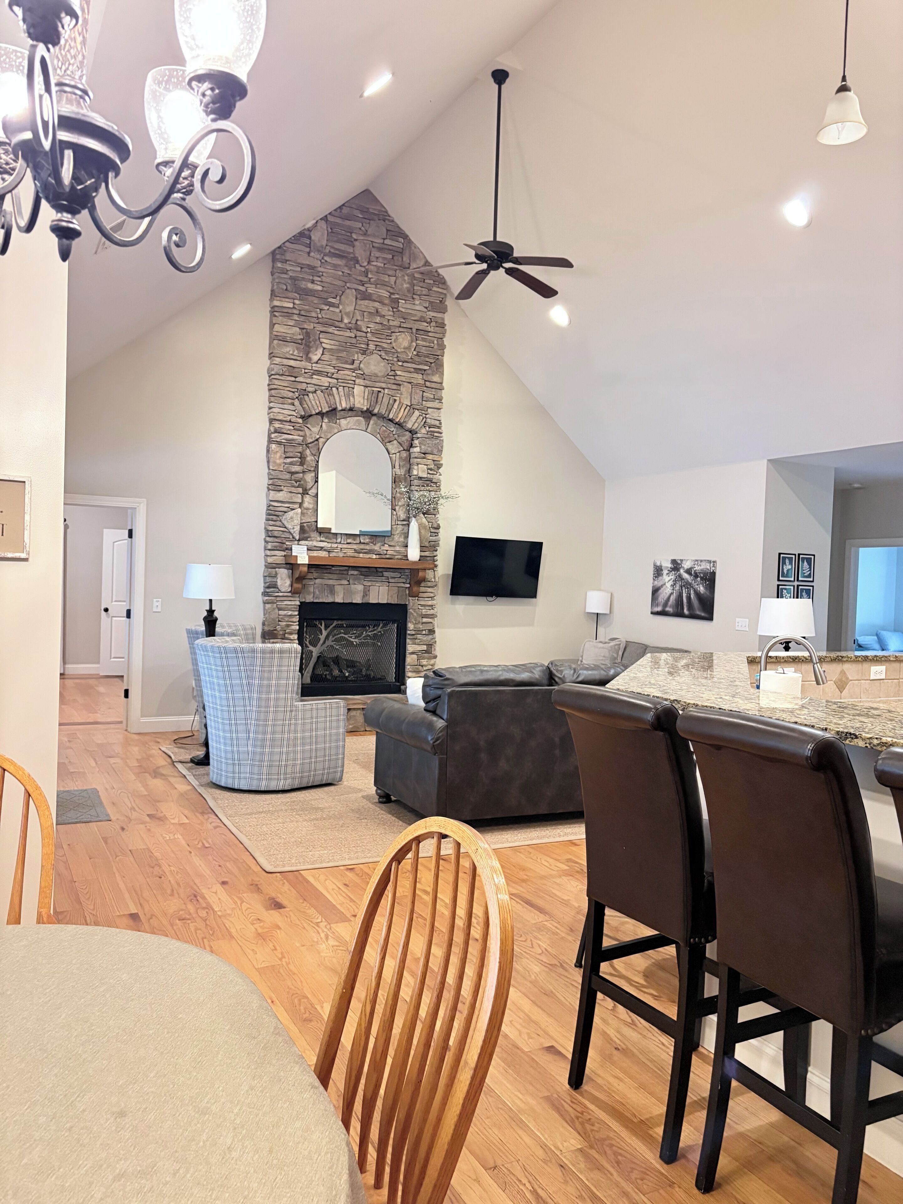 Una cocina moderna con chimenea de piedra, un comedor con sillas de madera y una sala de estar con sofá y televisor.