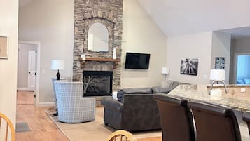 Una cocina moderna con chimenea de piedra, un comedor con sillas de madera y una sala de estar con sofá y televisor.