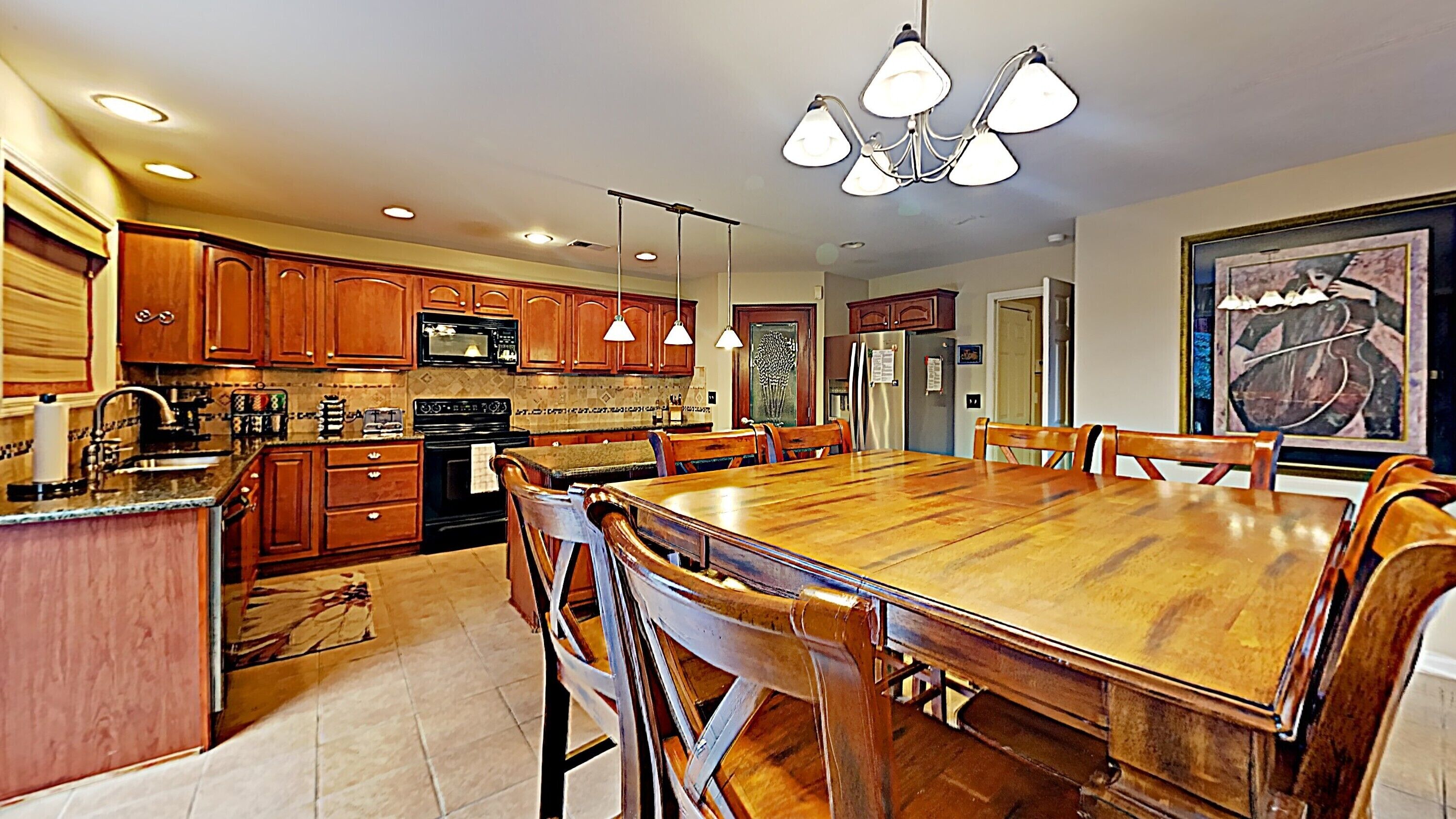 A kitchen with wooden cabinets, a large dining table, and pendant lighting.