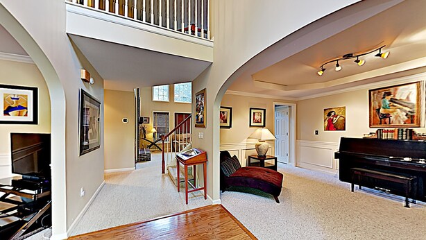 A spacious living room with a piano, a fireplace, and a staircase leading to an upper level. - Your Home Away From Home (Lexington)