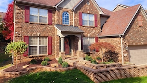 A two-story brick house with a front porch, a garage, and a landscaped front yard. - Your Home Away From Home (Lexington)