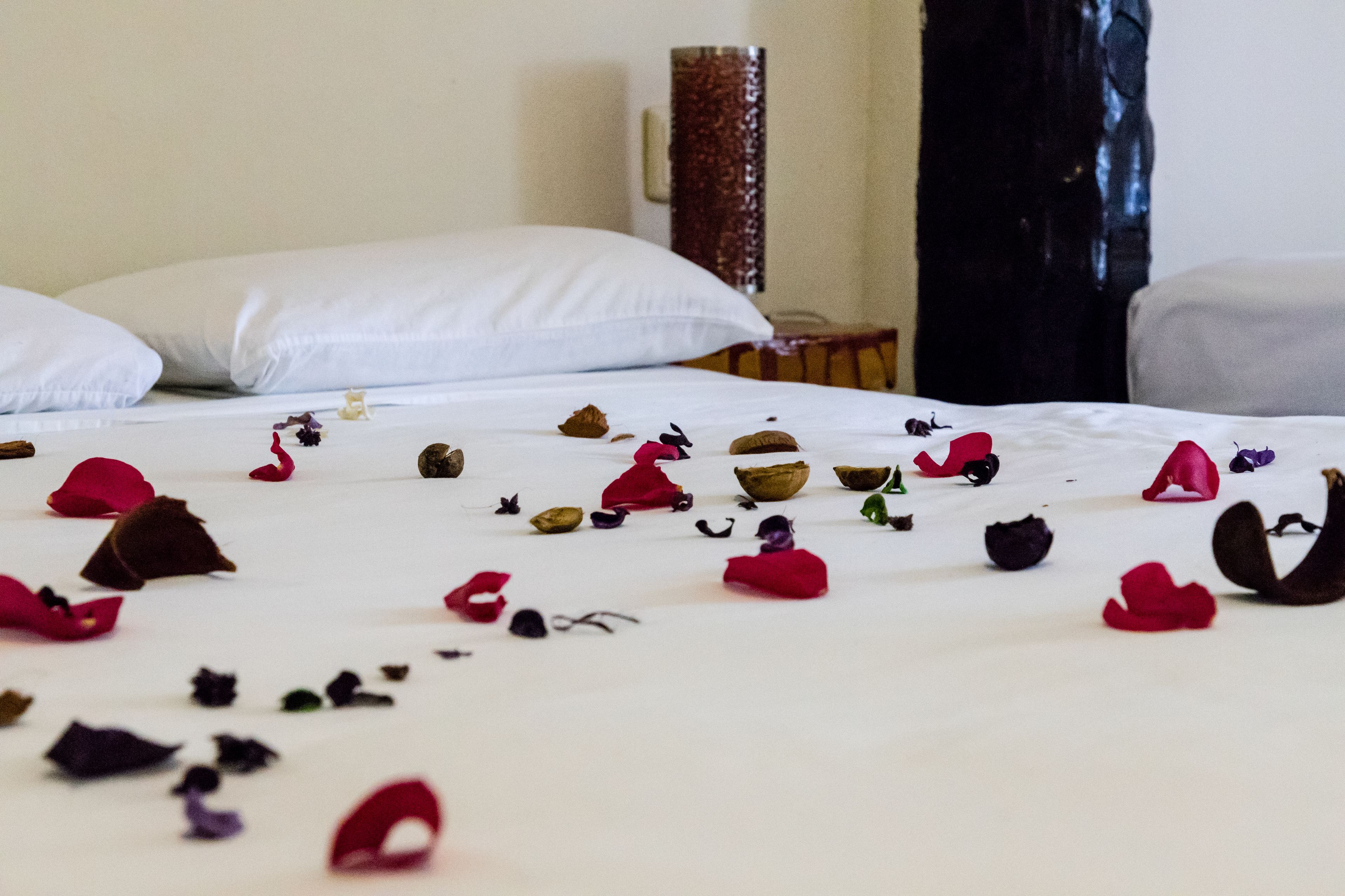Une chambre d’hôtel avec un lit soigneusement fait, des oreillers, ainsi que des pétales et des feuilles de fleurs éparpillées.