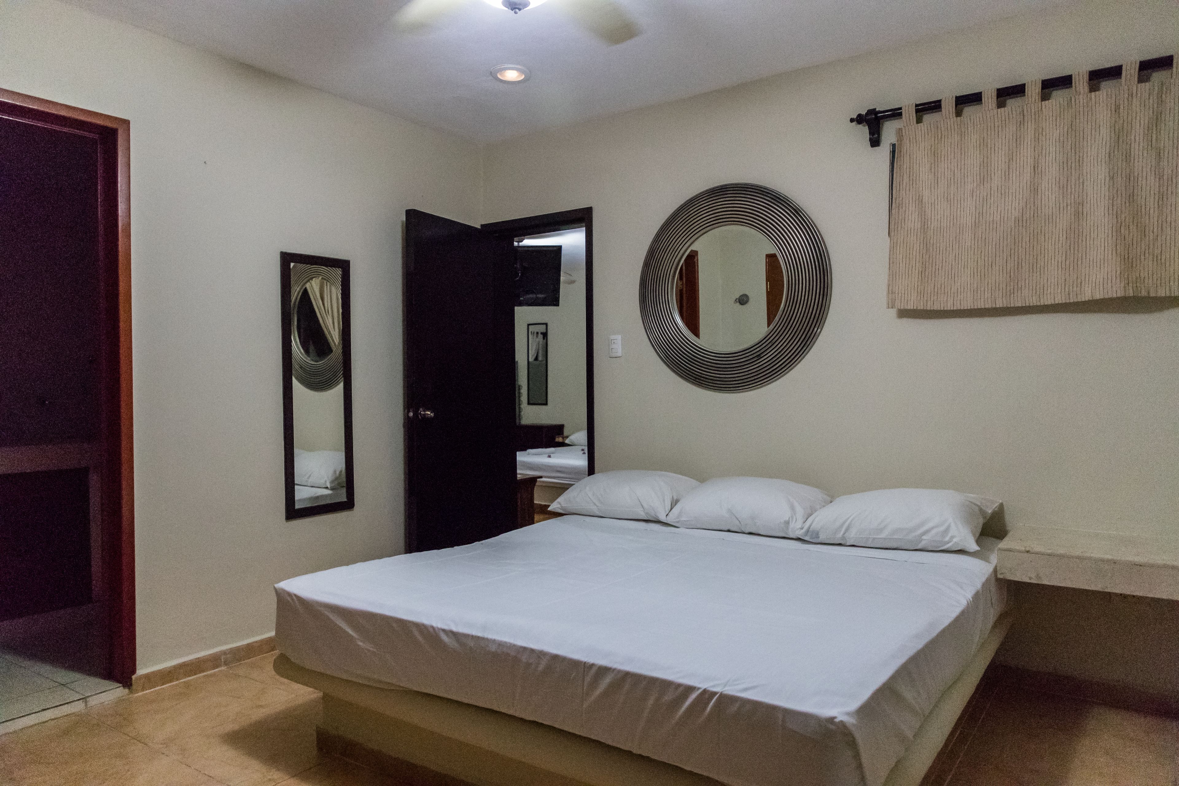 A bedroom with a bed, a door, a mirror, and a curtain.