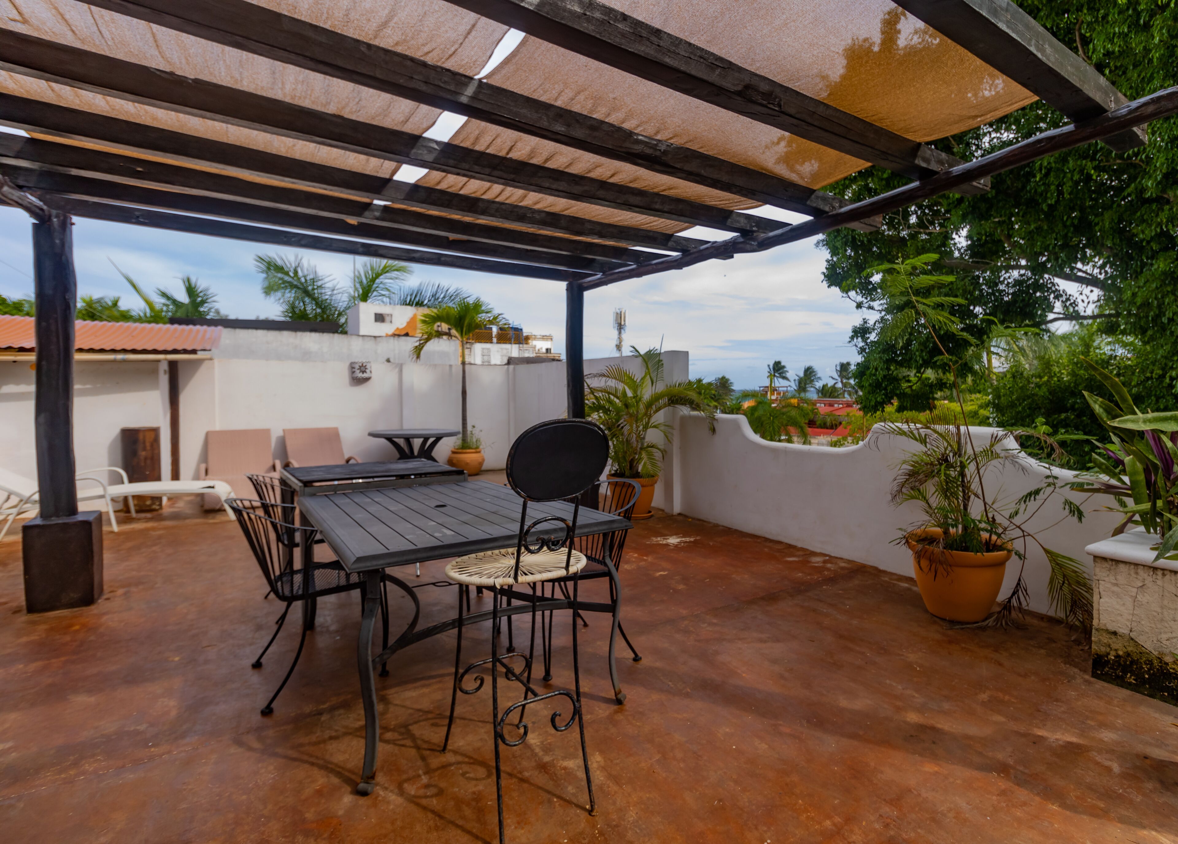 An outdoor patio with a table and chairs, surrounded by potted plants and a pergola.