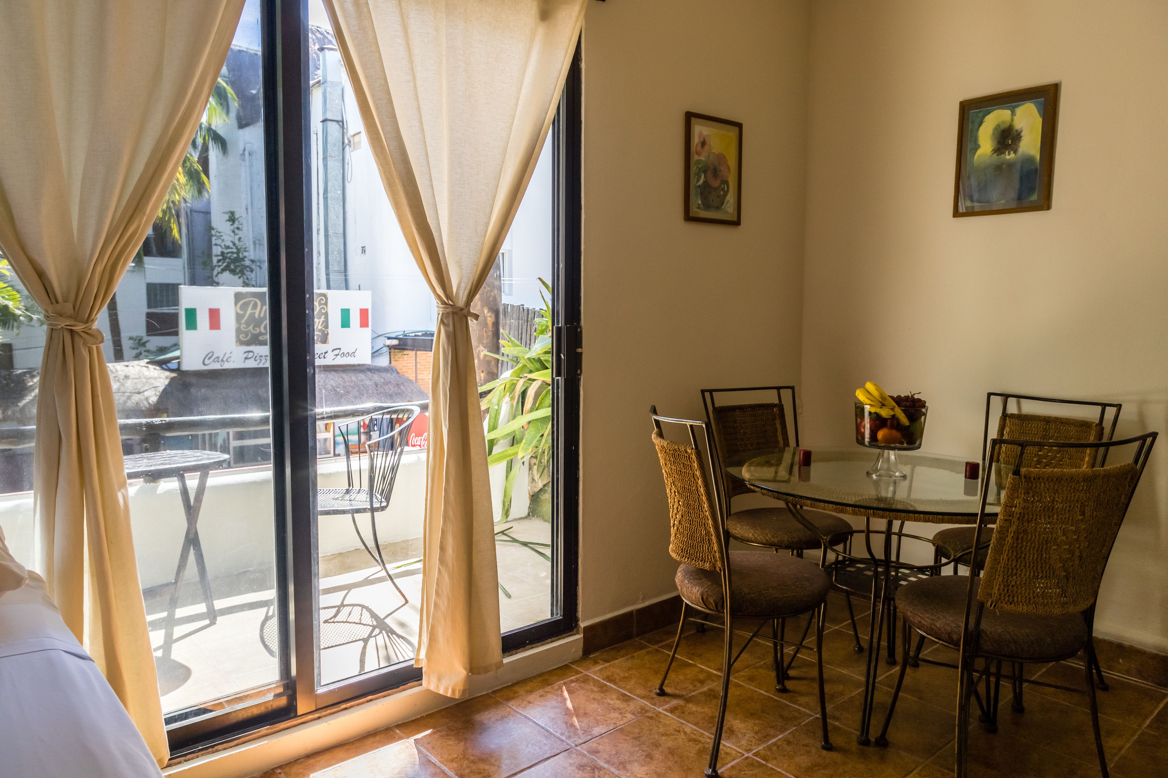 A dining area with a glass table and wicker chairs, a window with curtains, and a view of the street outside.