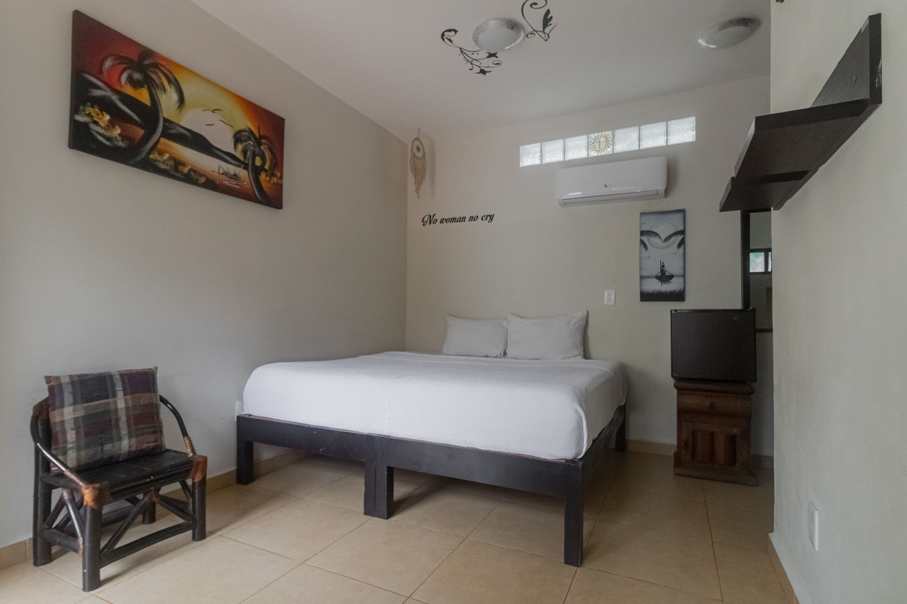 A bedroom with a bed, a chair, a painting, a wall decoration, and a television.