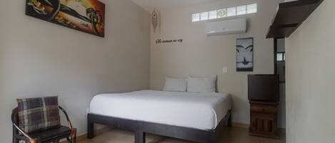 A bedroom with a bed, a chair, a painting, a wall decoration, and a television.