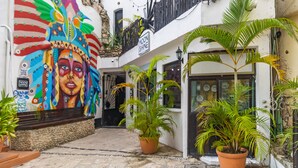 A narrow alley with a colorful mural on the left, a sign reading "MOON SHINE" on the right, and potted plants along the path. - Moonshine Hotel (Playa del Carmen)