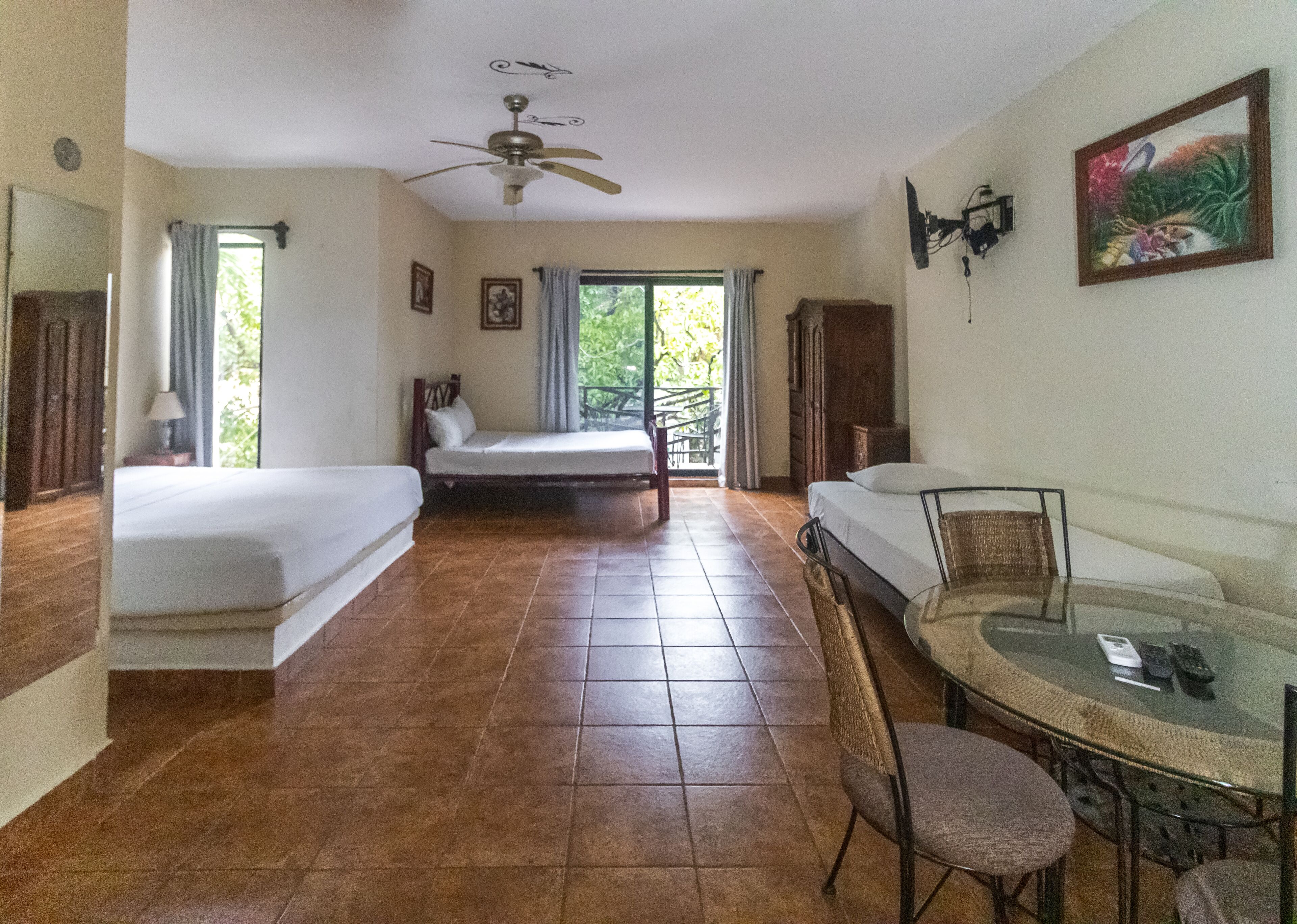 A hotel room with two single beds, a ceiling fan, a dining table with chairs, and a window with curtains.