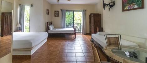 A hotel room with two single beds, a ceiling fan, a dining table with chairs, and a window with curtains.