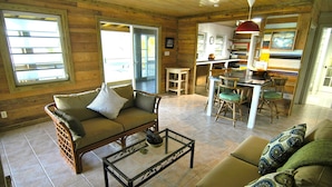 A cozy cabin interior with a wooden floor, a sofa, a coffee table, and a dining area with chairs and a table. - Peaceful Waterside Eco-Friendly Guest House on Stocking Island (Great Exuma)