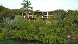 A coastal property with a two-story building, a balcony, and a view of the sea. - Peaceful Waterside Eco-Friendly Guest House on Stocking Island (Great Exuma)