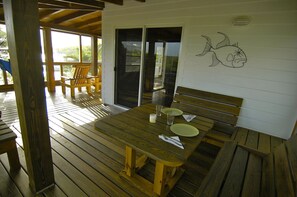 A wooden deck with a table set for two, a bench, and a wall with a fish drawing.
