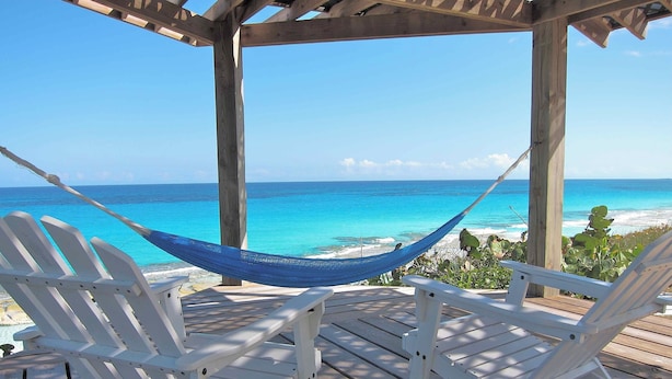 A wooden deck with white lounge chairs and a hammock overlooking a beach with clear blue water. - Peaceful Waterside Eco-Friendly Guest House on Stocking Island (Great Exuma)