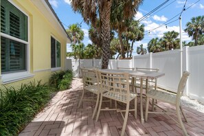 A patio with a table and chairs, surrounded by a white fence and palm trees. -  Cozy Cottage, 1 minute walk to Beach (Clearwater)