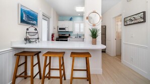 Una cocina moderna con armarios blancos, encimera blanca y tres taburetes de madera.