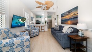 Una sala de estar moderna con sofá, sillones, televisor y ventilador de techo.