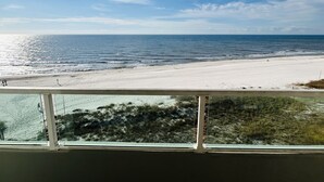 Uitzicht op een strand vanaf een balkon met een hekwerk, zee en heldere lucht.