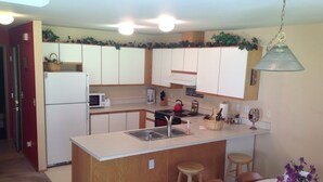A compact kitchen with white cabinets, a central island with stools, a microwave, a kettle, and a fan. - Welcome to the Bean's Pod :-) (Leavenworth)