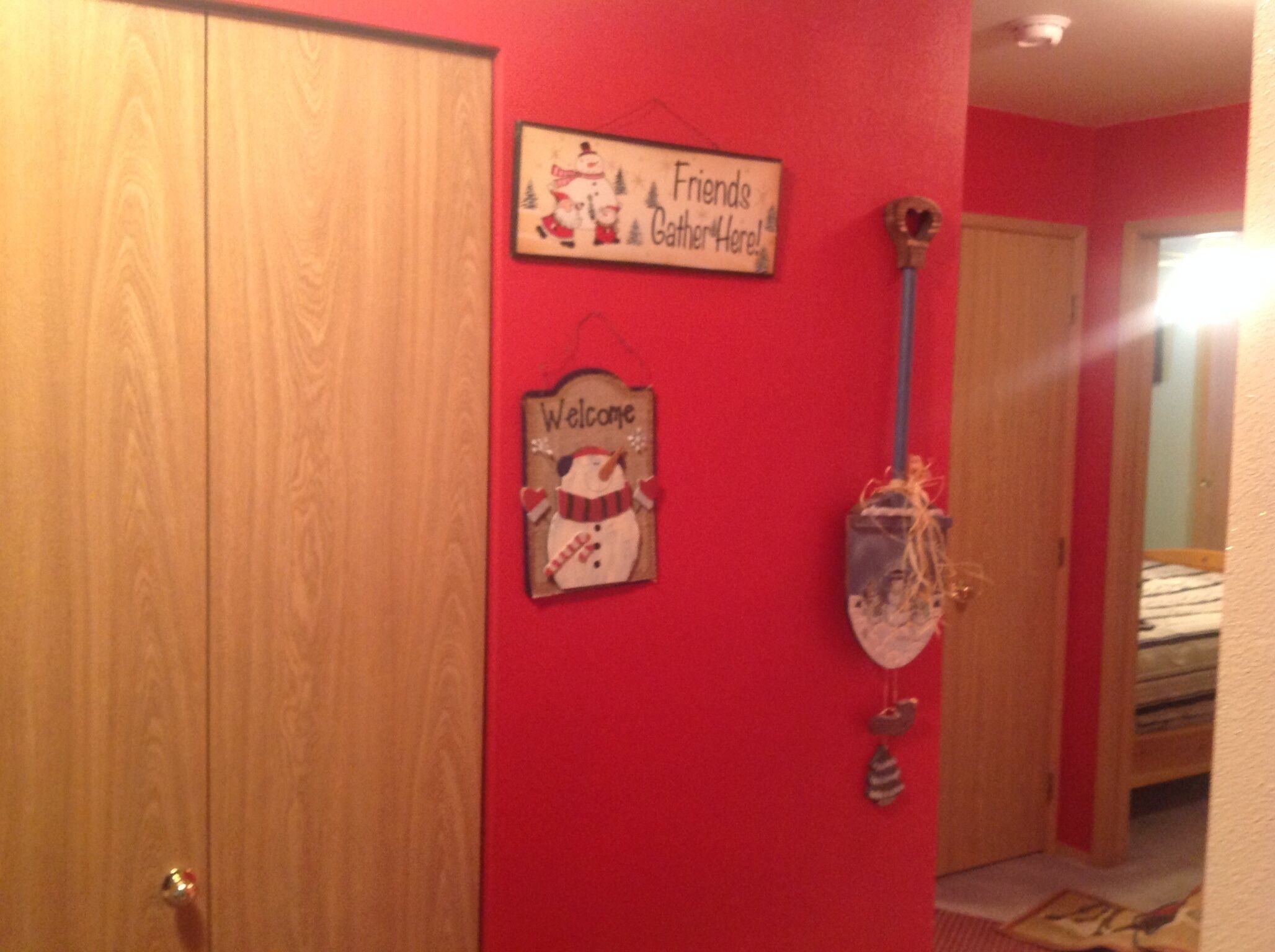 A room with a red wall, a wooden door, and a sign that says "Friends Gather Here!"