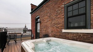 A hot tub on a wooden deck with a brick wall and a window. - Drake House: City View (Private Hot Tub) (Dubuque)
