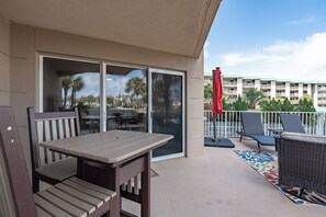 A balcony with a table and chairs, a red umbrella, and a view of a building with balconies.