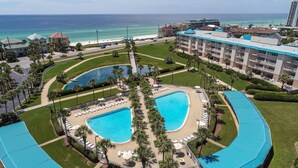 A resort with two large swimming pools surrounded by palm trees and lounge chairs, overlooking a beach and ocean. - Aug/Sept Openings SAVE Large Walk Off  Patio w/Grill. 2 Pools, Beach Service!!!! (Miramar Beach)