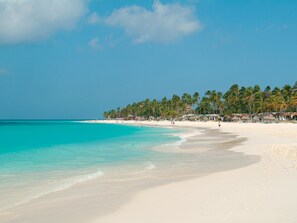 A beach with clear turquoise water, white sand, and palm trees.