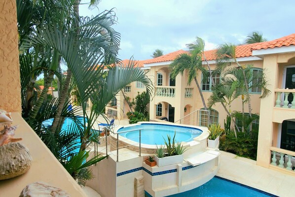 A pool area with a hot tub, surrounded by palm trees and a building with a tiled roof.
