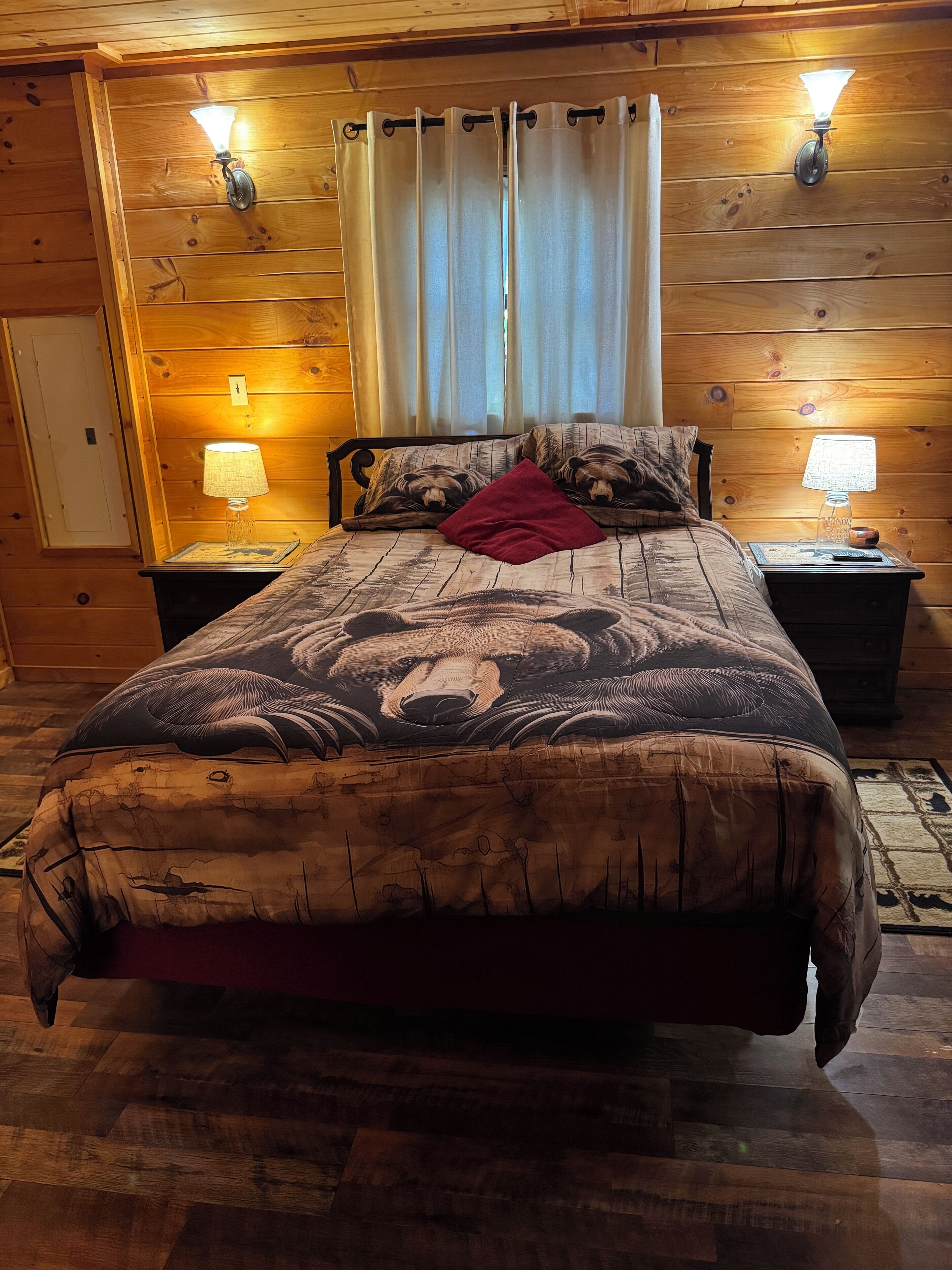 A wooden-paneled room with a bed, two bedside lamps, and a window with curtains.