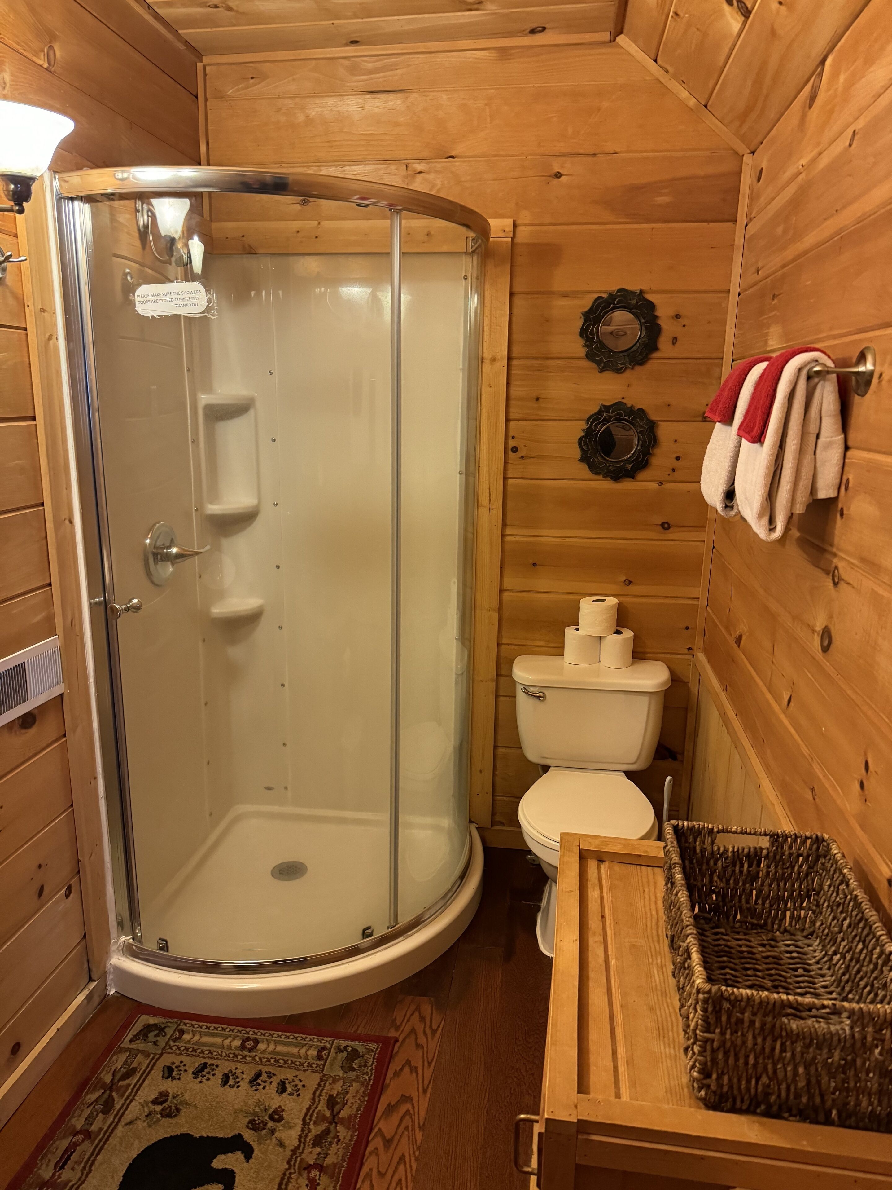 A wooden cabin bathroom with a glass shower enclosure, a toilet, and a wicker basket.