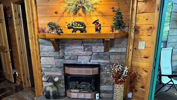 Interior de madera con chimenea de piedra, repisas de madera con adornos y un suelo con motivo de espiga.