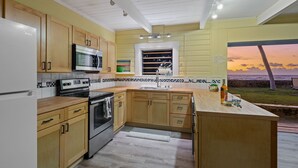 A modern kitchen with wooden cabinets, stainless steel appliances, and a view of the ocean at sunset. - Oceanfront Hawaiian-style Beach House (Waimea)