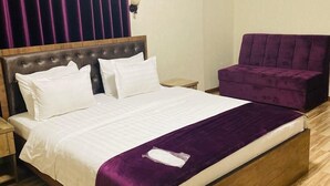 A neatly made bed with white linens and a purple throw blanket, a wooden headboard, and a wooden nightstand with a lamp. - Tourist INN Hotel (Tashkent)