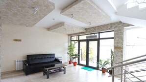 A spacious living area with a black sofa, a coffee table, and potted plants. - Tourist INN Hotel (Tashkent)