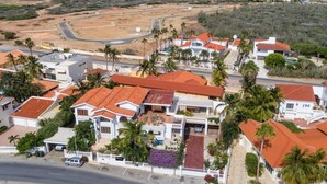 Zona residencial con casas de techo rojo y tejado de tejas, rodeada de palmeras y una calle.