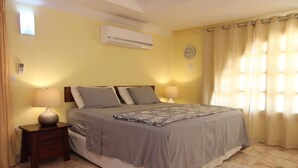 Un dormitorio con una cama, dos mesitas de noche, una lámpara, aire acondicionado y una ventana con cortinas.