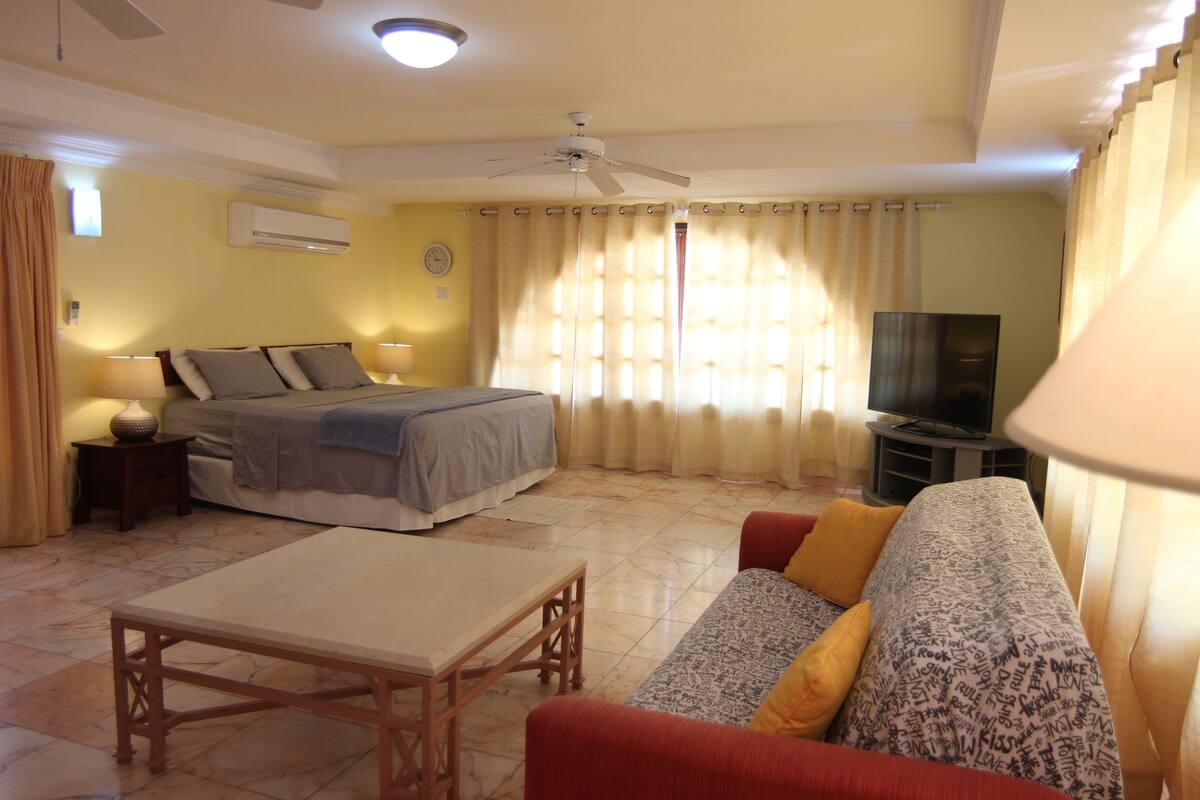 A hotel room with a bed, a TV, a sofa, a table, and curtains.