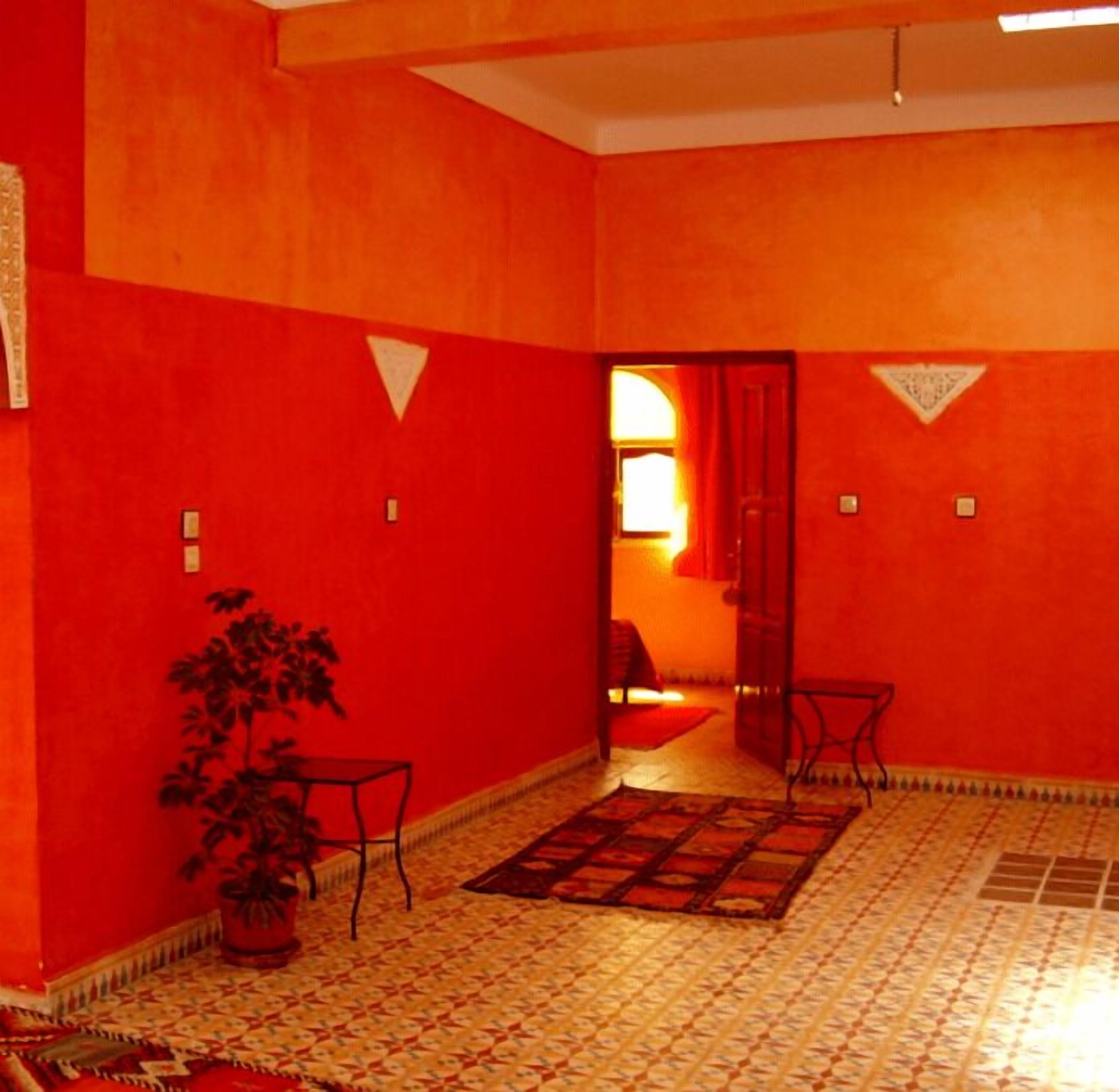 Una habitación con paredes rojas, suelo de baldosas, una planta en maceta y una pequeña mesa.