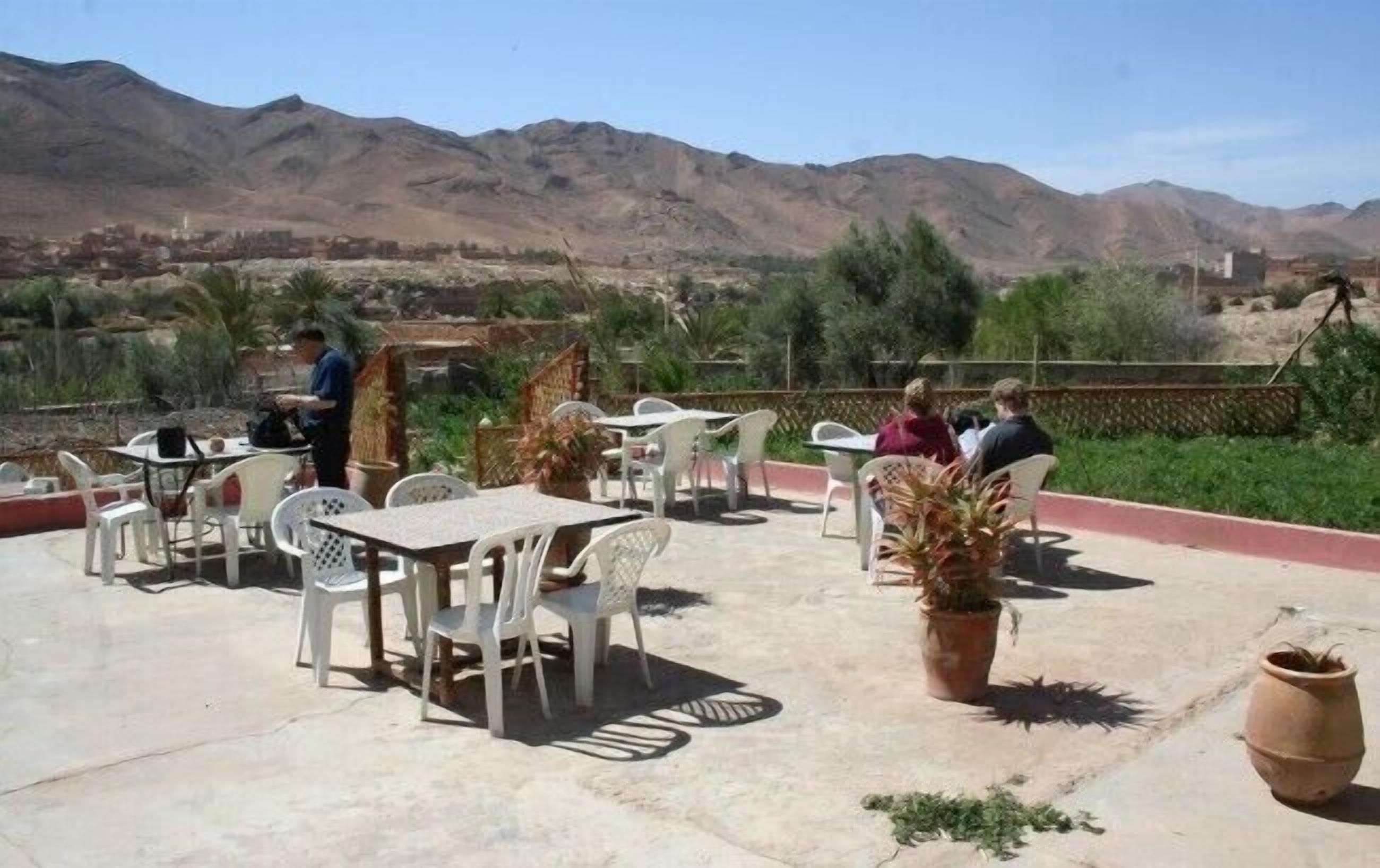 An outdoor patio with tables and chairs, surrounded by potted plants and a view of mountains.