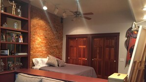 A bedroom with a brick wall, a bed, a wooden dresser, and a desk with a computer.