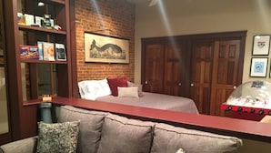 A room with a brick wall, a bed with a white and red blanket, a wooden door, and a red table with a glass top.