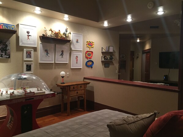 Una habitación con cama, un escritorio con un globo terráqueo, estanterías con figuritas, cuadros enmarcados y un televisor.