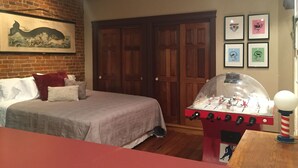 A bedroom with a bed, a futon, a foosball table, and a ceiling fan.
